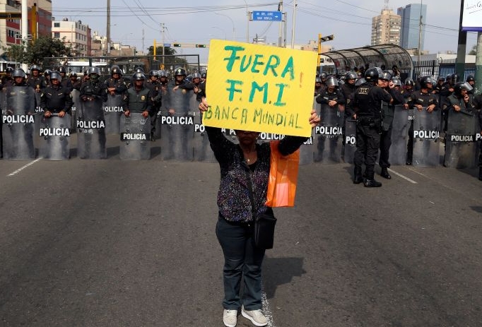 A protester holds a sign that reads, in Spanish, ‘Get out IMF, World Bank’, Lima, Peru, Friday, October 9, 2015
